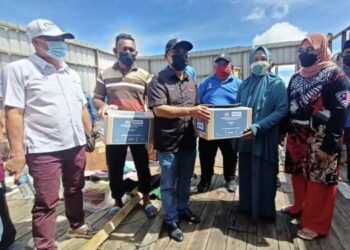 RONALD Kiandee (tiga kiri) menyampaikan bantuan bakul makanan kepada salah seorang penerima di Kampung Pulau Keniogan, Beluran semalam.