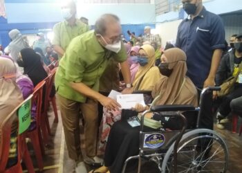 WAN ROSDY Wan ismail (kiri) bertanyakan khabar dan menyampaikan duit raya bernilai RM700 kepada seorang penduduk, Aziah Hassan (berkerusi roda) di Kuala Lipis di Lipis, Pahang. - UTUSAN/HARIS FADILAH AHMAD