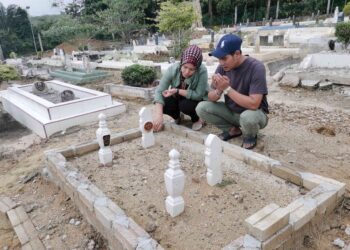 MOHD. Fazlan Nizam dan Mimi Doleng menziarahi kubur anak mereka di Tanah Perkuburan Islam Kampung Bali dekat Seri Iskandar di Parit, Perak. – UTUSAN/AIN SAFRE BIDIN