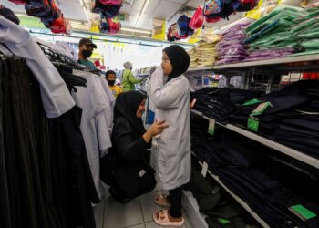 Seorang wanita memilih baju sekolah untuk anaknya di sebuah pasar raya di Jalan Tuanku Abdul Rahman, Kuala Lumpur, semalam menjelang pembukaan sesi persekolahan Isnin ini. – UTUSAN/FARIZ RUSADIO