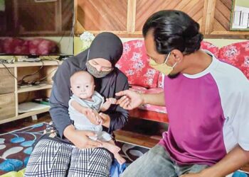 SAH Rizal Mohamed Aripin memerhatikan anaknya, Mohd. Az-Ziqri didukung isterinya, Norizan Mohd. Jais dekat kediamannya di Kampung Parti 13, Sungai Panjang di Sabak Bernam, Selangor.