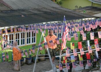 RAHMAH Mohd. Noor dan suami, 
Ahmad Sabri Hashim memasang Jalur Gemilang di pekarangan rumah mereka di Felda Tersat, Hulu Terengganu, hari ini. - PUQTRA HAIRRY ROSLI