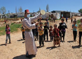 KANAK-KANAK di kem pelarian Syria di Lubnan menyaksikan persembahan oleh seorang lelaki. Sembilan daripada 10 pelarian Syria di Lubnan hidup dalam kemiskinan, ada yang mengambil keputusan untuk kembali ke negara asal mereka. - AFP