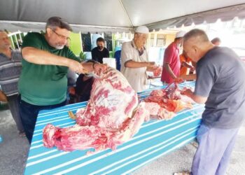 ASWANE Zulkifli Strok (kiri) melapah daging korban sambil dibantu penduduk di Jalan Nirwana 12, Klebang, Melaka. - UTUSAN/AMRAN MULUP