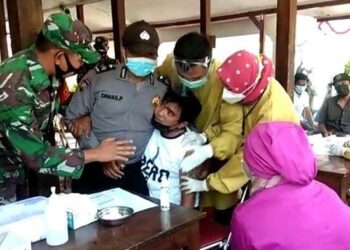 Lelaki bertatu di Wonogiri , Bali takut disuntik vaksin sehingga perlu dipegang banyak petugas. - Foto Tribunenews