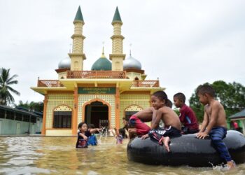 KANAK-KANAK bermain air banjir di hadapan masjid selepas hujan lebat melanda daerah Ra-ngea di wilayah selatan Thailand, Narathiwat. -AFP