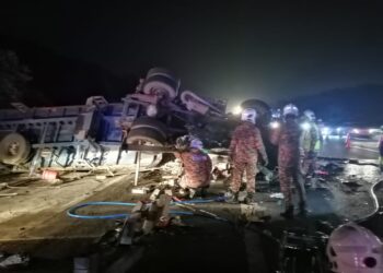ANGGOTA bomba mengeluarkan pemandu treler yang tersepit dalam kemalangan di Kilometer 371.7, Lebuh Raya Utara-Selatan arah selatan dekat Tanjung Malim semalam. - UTUSAN/JBPM PERAK