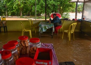 SEORANG penduduk bersarapan di kedai makan yang turut dinaiki banjir di Kampung Nibung, Hulu Terengganu, hari ini. - FOTO/PUQTRA HAIRRY ROSLI
