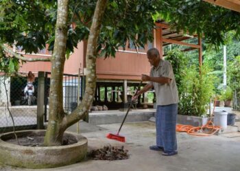 WAN Omar Wan Ahmad membersihkan halaman rumah bagi menunggu kepulangan anak dan cucu di Kampung Sekati di Kuala Terengganu, semalam. - PUQTRA HAIRRY ROSLI