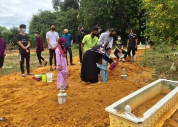 ROSFAZILAH Salleh menyiram air di pusara anaknya di Tanah Perkuburan Kampung Bukit Berangan di Kuala Nerus, Terengganu, hari ini.