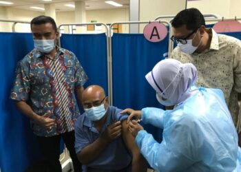 MOHAMAD Rafiq Mohd. Kasri (kiri) dan Mohd. Syahbuddin Hashim melihat pemberian suntikan vaksin kepada seorang penduduk di PPV Pusat Latihan Kesedar di Gua Musang, Kelantan. - UTUSAN/AIMUNI TUAN LAH