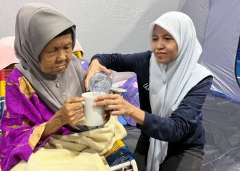 NORISAN ALI membantu menyiapkan keperluan ibunya ketika ditempatkan di PPS di IKTBN Pagoh, Muar.
