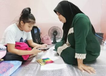 Anuma (kanan) membantu anak sulungnya menyiapkan kerja sekolah yang diberikan melalui sesi PdPR di Dewan DSP Mohd Dun Banir, Beaufort Sabah.