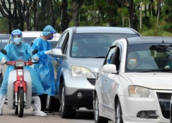 DUA orang petugas kesihatan menaiki motosikal bagi mengedarkan borang maklumat kepada pemandu kenderaan yang akan menjalani ujian calitan di OSCAC di Stadium Tertutup MBPG di Pasir Gudang, Johor. -UTUSAN/RAJA JAAFAR ALI