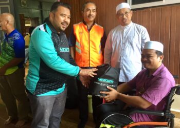 TUAN Kamarul Arief Tuan Soh (kiri) menyampaikan bantuan kepada seorang mangsa banjir OKU di Kuala Nerus, Terengganu, hari ini. - UTUSAN/TENGKU DANISH BAHRI TENGKU YUSOFF